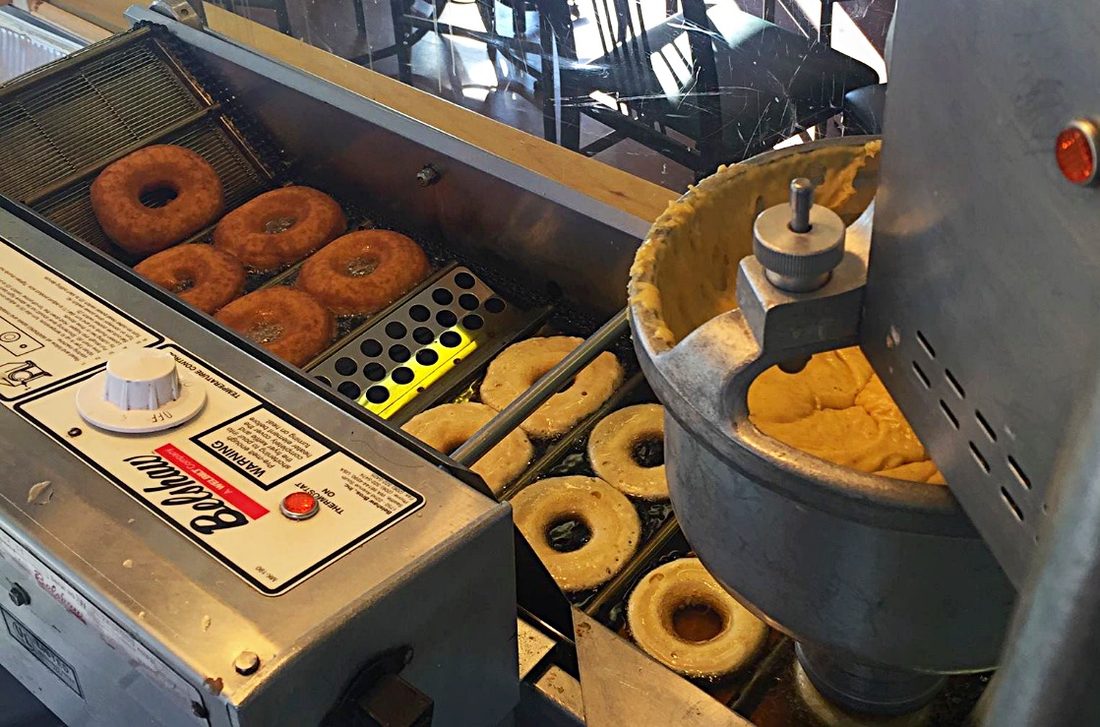 Cake donuts dropping into the fryer on the donut machine