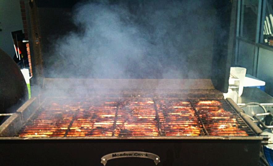 Ribs cooking over the coals in the Meadow Creek smoker with smoke rolling out